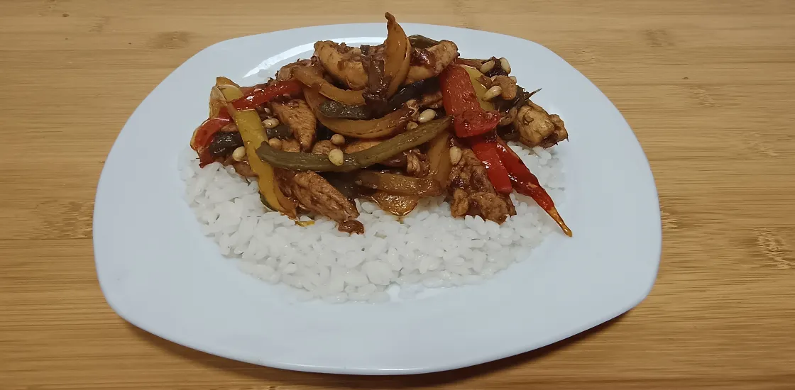 Un plato de salteado de pollo con pimientos y piñones